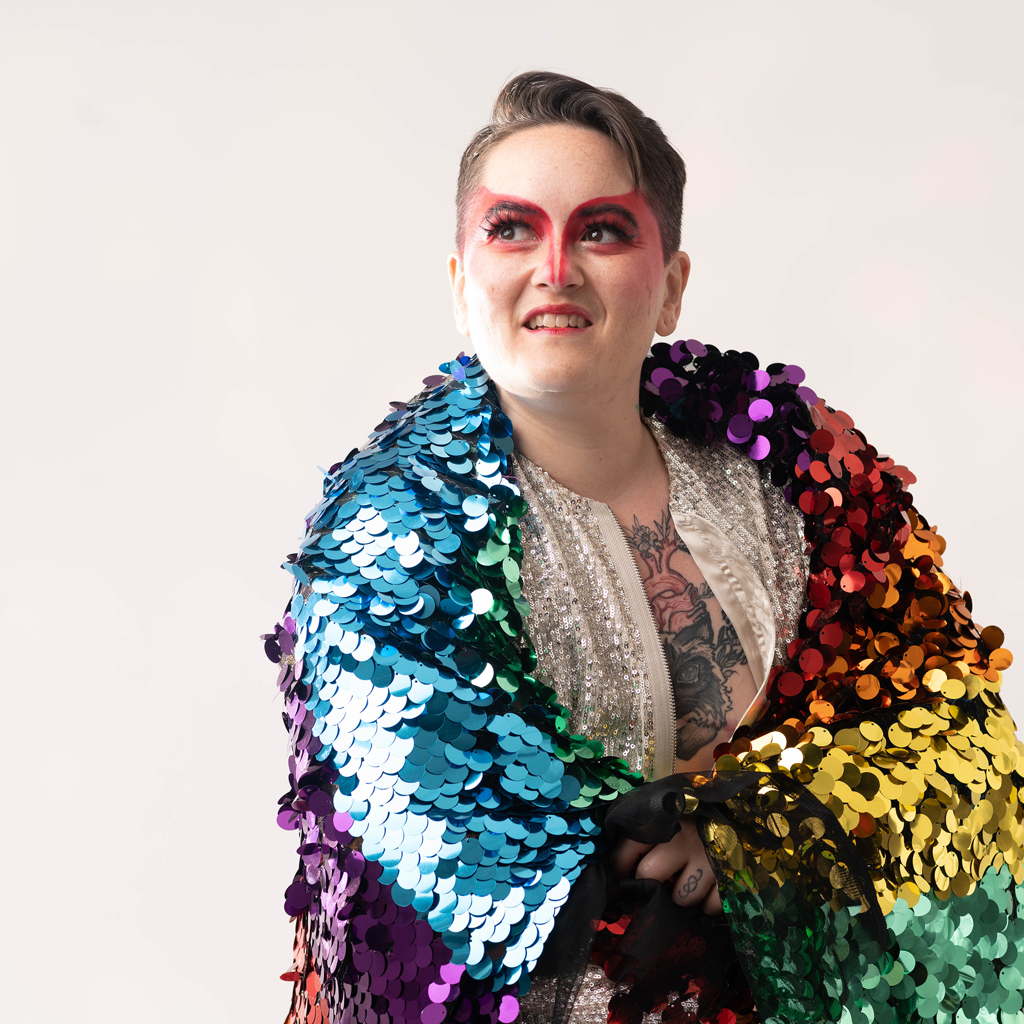 Chris wearing kabuki-style red eye makeup and draped in a rainbow colored sequin blanket